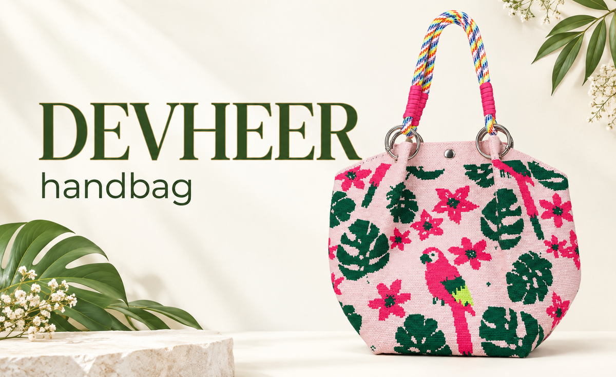 A pink woven tote bag with a tropical print featuring green monstera leaves, pink flowers, and a pink parrot, complete with colorful braided rope handles and silver metal rings, set against a neutral linen background.